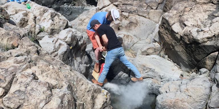 Two men using mechanical equipment to break up rocky landscape
