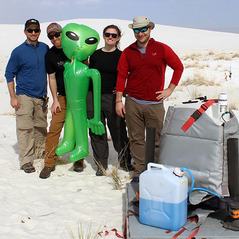 Four people out in the field posing with a blow-up alien