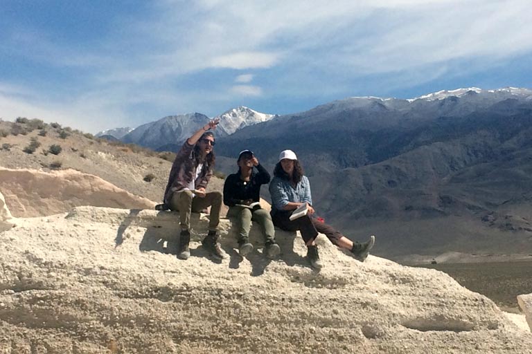 Three students sitting in a mountainous location