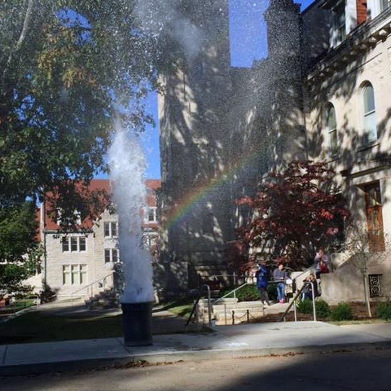 Water exploding out of a trashcan and creating a rainbow in the sunlight