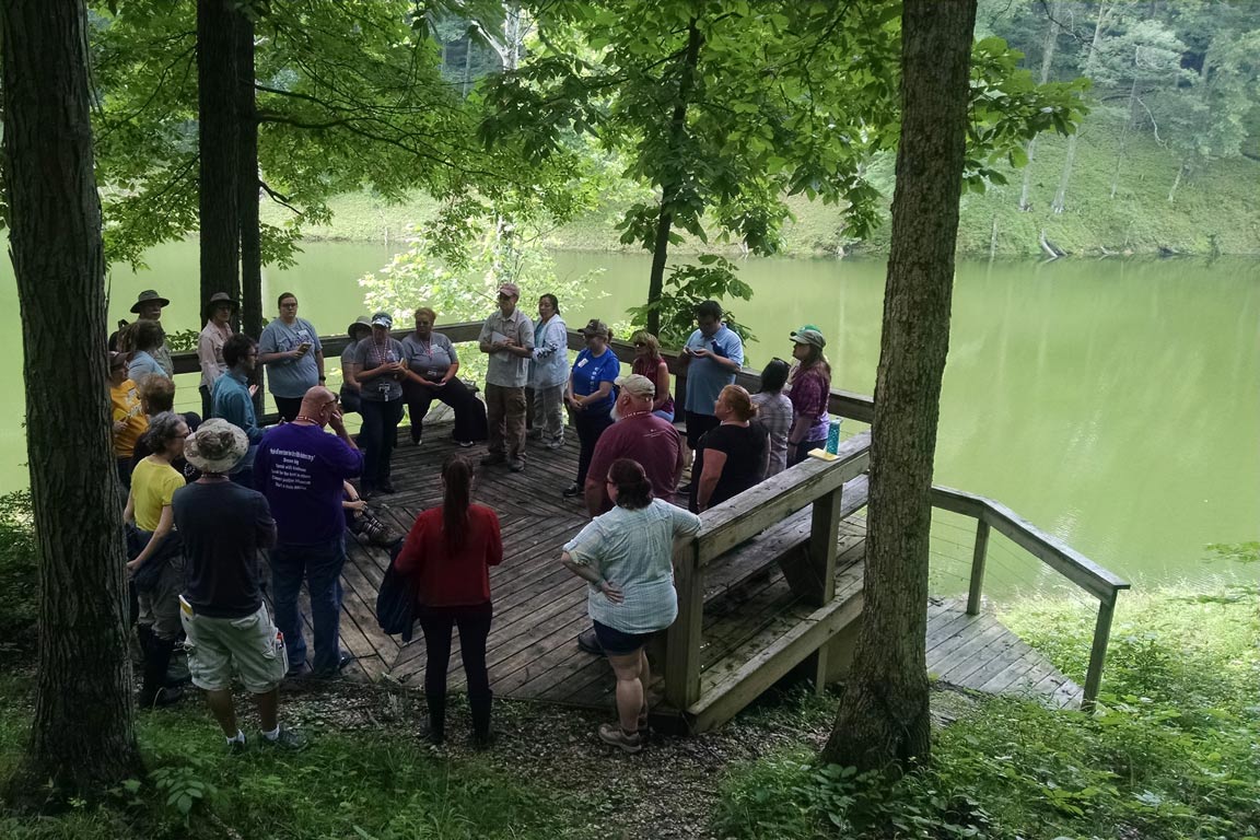 Large group of people standing on a deck alongside a river