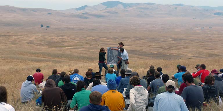 Group of students and teachers analyze a map with Montana terrain in the background
